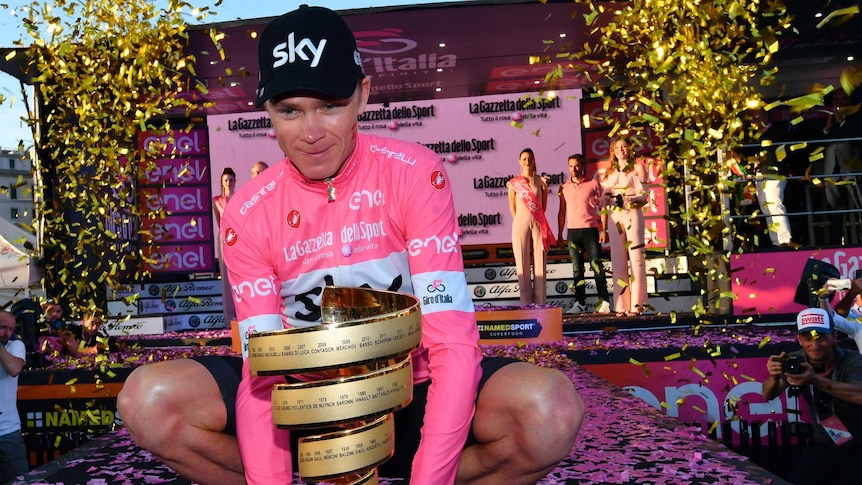 A rider wearing a pink jersey poses on one knee with the trophy of the Giro d'Italia cycling race.