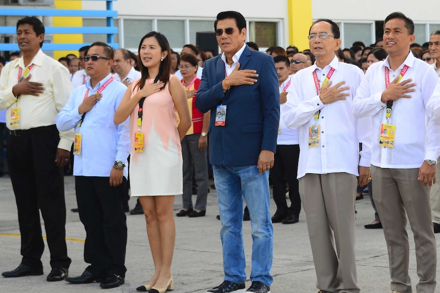 Antonio Halili stands with his hand on his chest alongside other dignitaries during a flag-raising ceremony.
