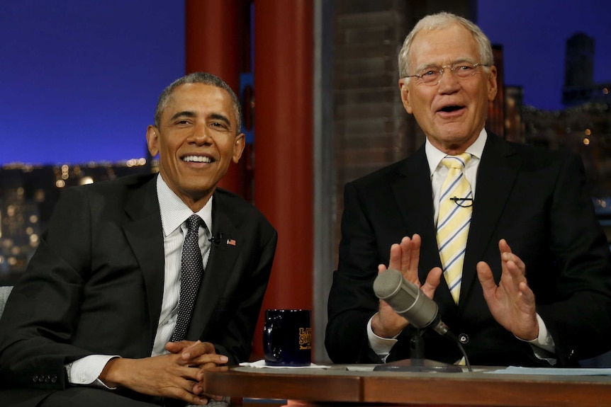 Barack Obama sits with David Letterman on The Late Show set both smiling looking into crowd