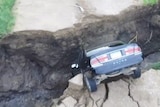 View from above, looking down at a sedan face down in the sinkhole, with only its rear tyres and boot above ground level.