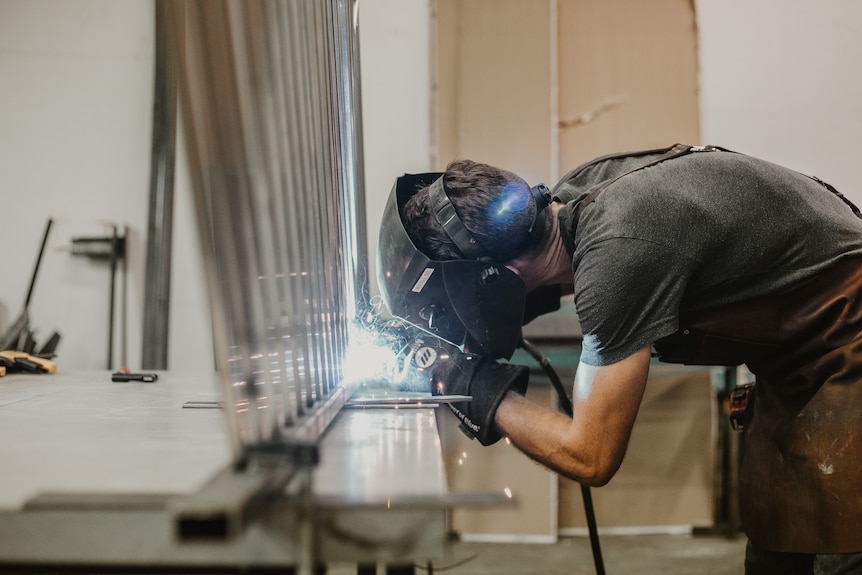 A man wearing a welding helmet uses a tool with sparks flying