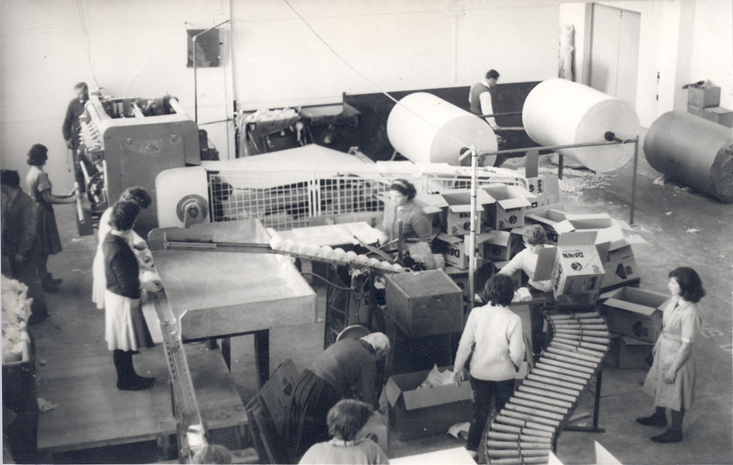 Mulheres em volta de máquinas de embalagem.