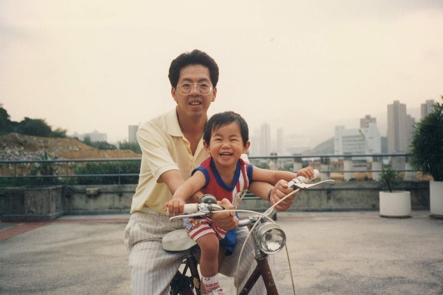 An old photo of Curtis Cheng holding his son Alpha Cheng on a bicycle.