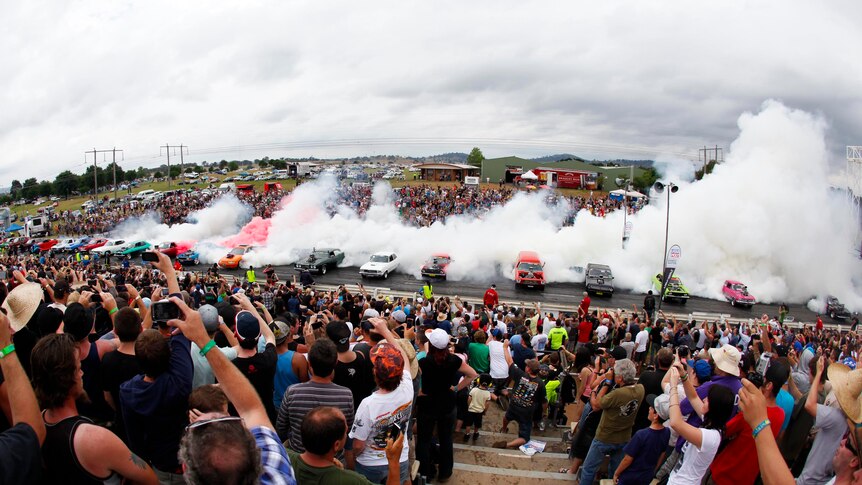 Spectators cheer as 22 cars perform a simultaneous burnout at the Summernats.