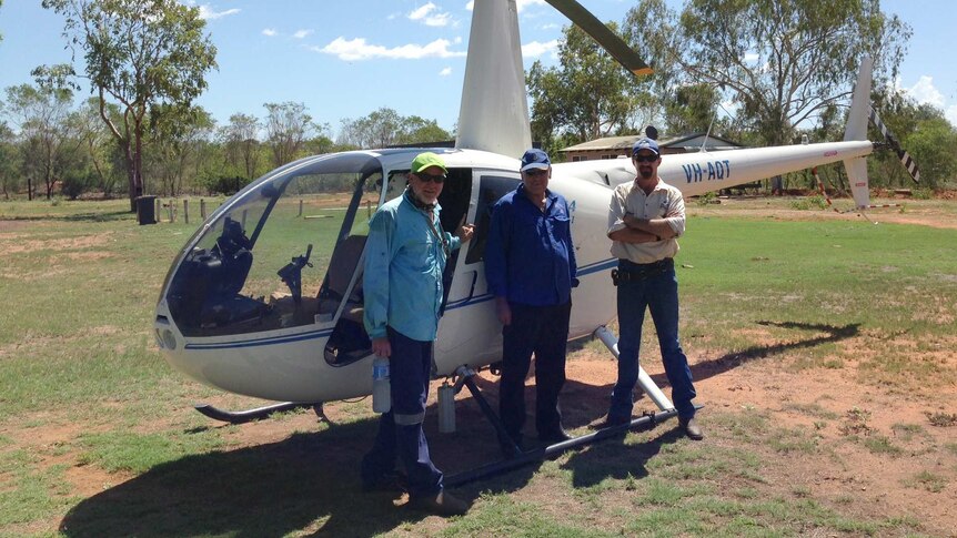 Three men from team Rubbervine stand alongside a white helicopter.