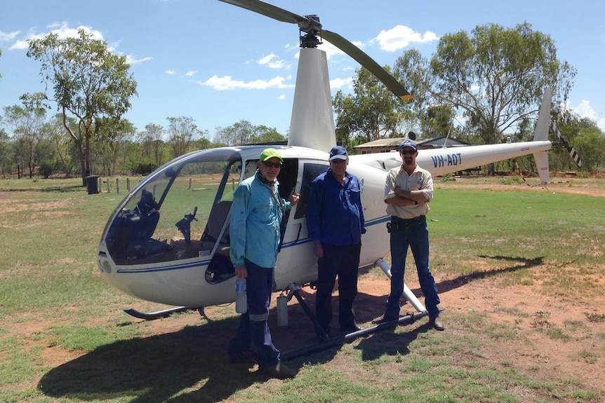 Three men from team Rubbervine stand alongside a white helicopter.