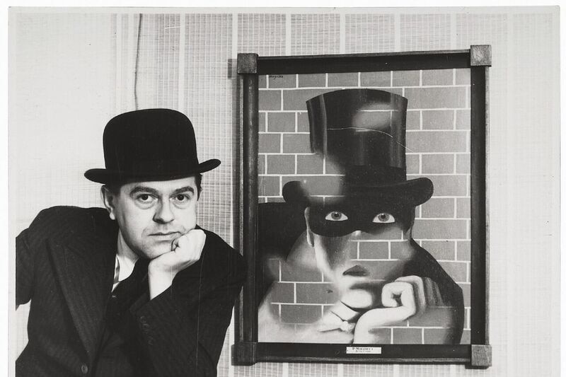 A man wearing a bowler hat poses next to a surrealist painting of a man in a top hat.