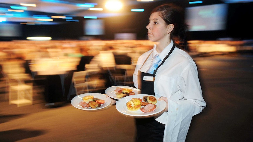 A waitress mid-stride holding three plates in her hands with a napkin over her left arm.