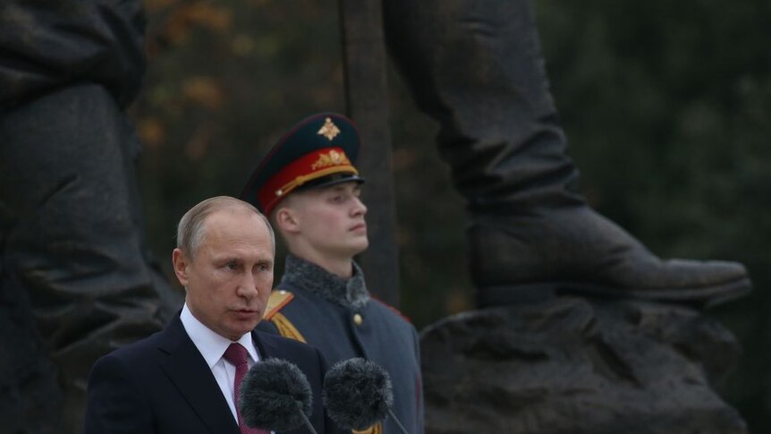 President Putin speaks with a uniformed soldier beside him.