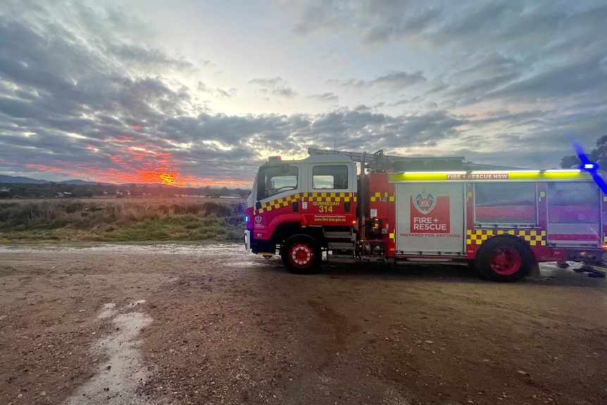 A fire truck is pictures against a picturesque sunset in a rural area