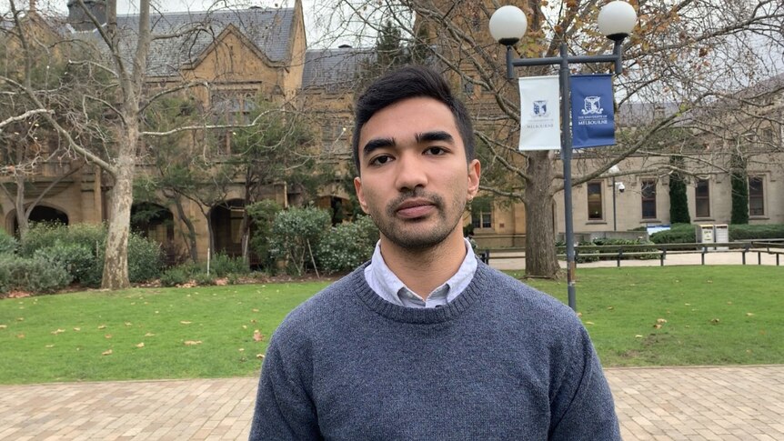 A picture of an Indian man with short dark hair on Melbourne's South Lawn with sandstone buildings in the background.