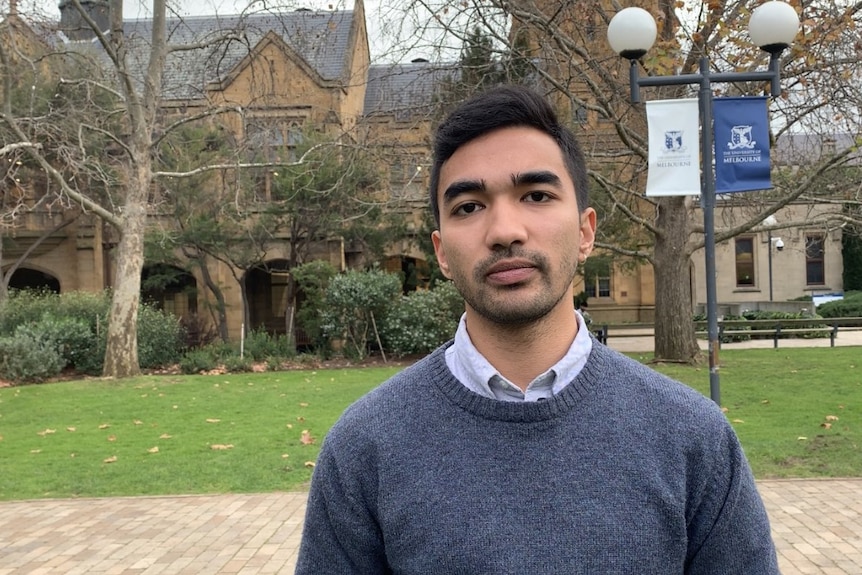 A picture of an Indian man with short dark hair on Melbourne's South Lawn with sandstone buildings in the background.