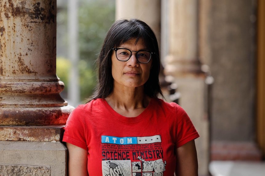 Dr Michelle Aung Thin wears a red T-shirt, standing next to a pillar 