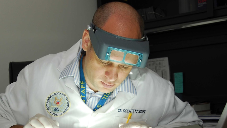 A man in a white lab coat looks closely as small x-rays on a horizontal lightbox.