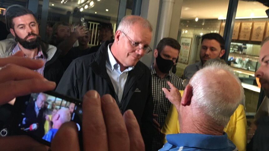 A balding man points at Prime Minister Scott Morrison who is surrounded by people inside a pub.
