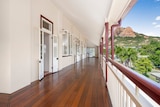 The verandah of a Queenslander with open French doors and a mountain, Castle Hill, in the background. 