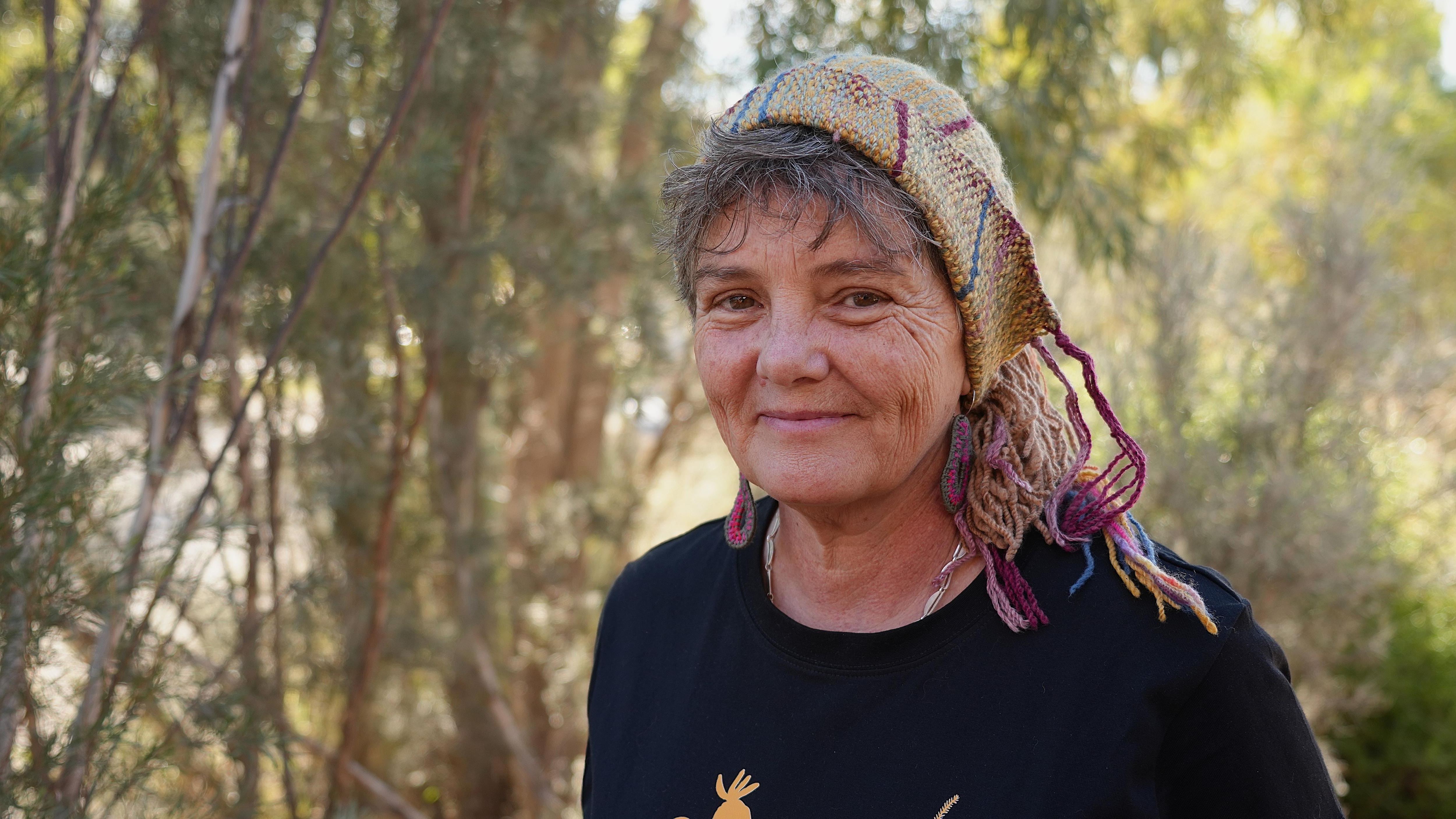 A woman smiling at the camera, she is wearing a colourful knitted beanie.