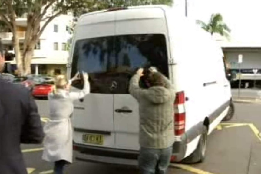 Journalists hold cameras up to the rear window of a large white van.