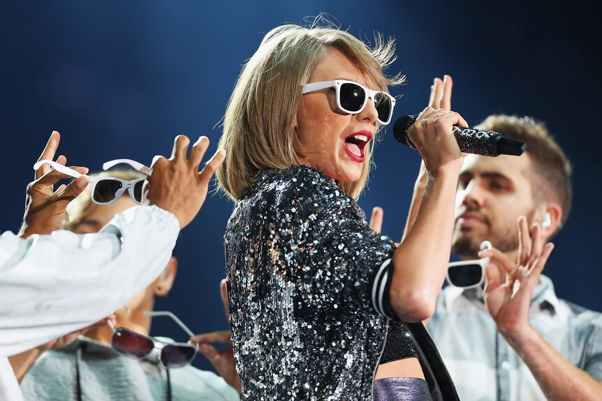 Taylor Swift performs on stage wearing sunglasses.