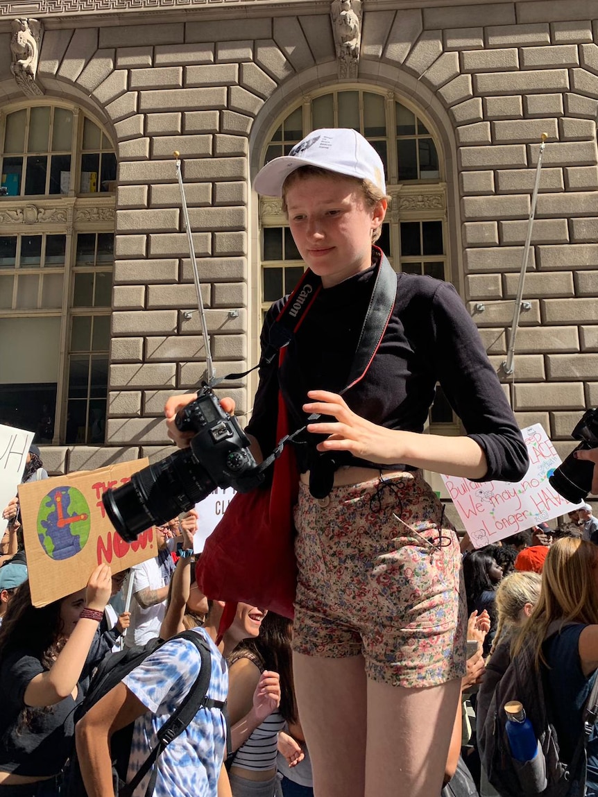 Harriet O'Shea Carre holds a camera as protestors walk past