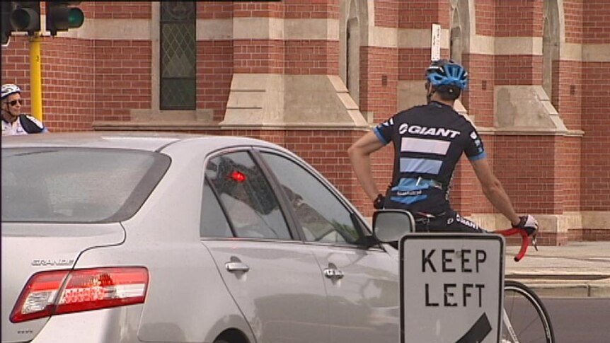A cyclist is stopped in the CBD next to a car.jpg