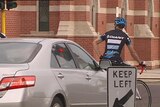 A cyclist is stopped in the CBD next to a car.jpg