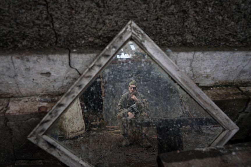 A Ukrainian serviceman is reflected in a mirror as he smokes a cigarette.