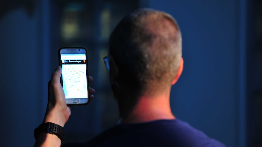 A man looks at the power outages on his phone during a blackout.