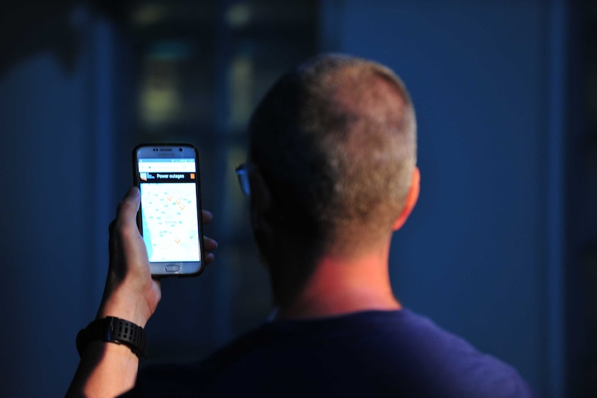 A man looks at the power outages on his phone during a blackout.