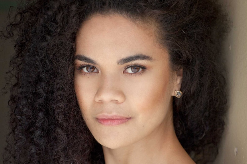 Akina Edmonds headshot. A woman with curly hair wearing an off shoulder black top.