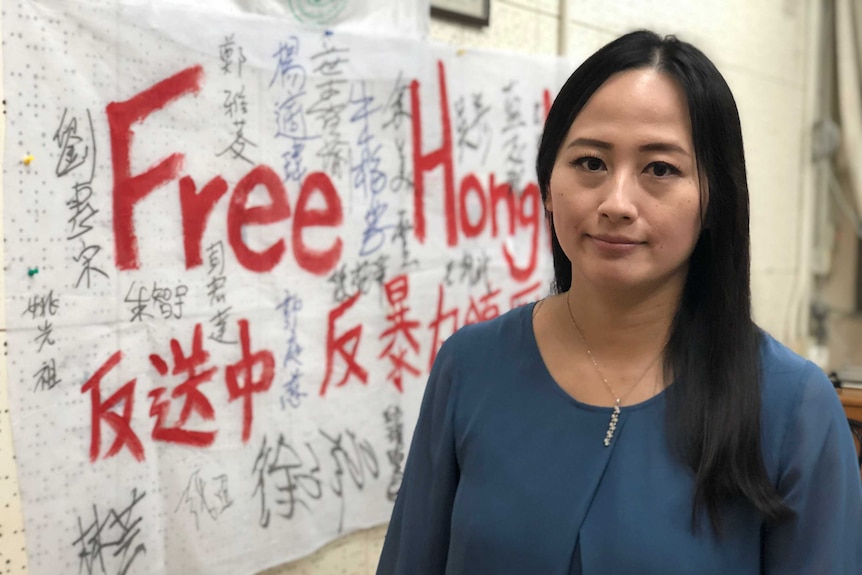 Rebecca Sy stands in front of a banner which says Free Hong Kong.