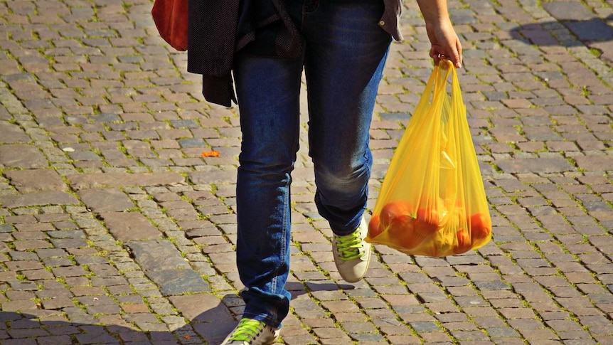 Image of person with blue jeans carrying a yellow shopping bag