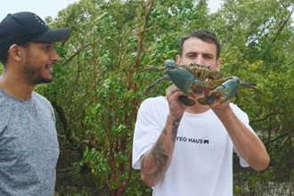 One man smiling at another man holding a mudcrab