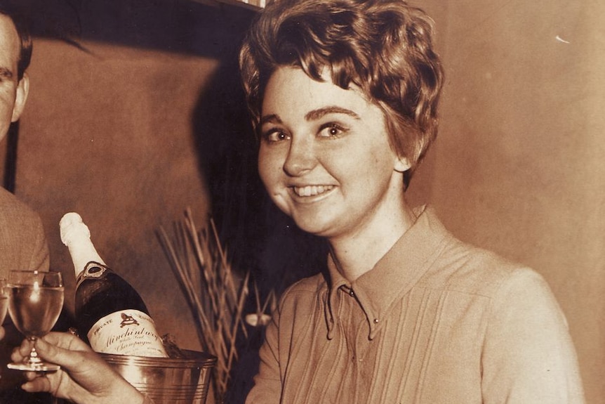 An old black and white photo of a woman holding a glass of wine smiling at the camera