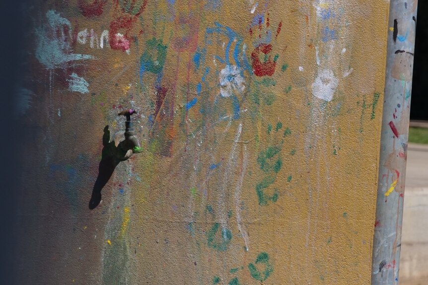 A tap in a wall with paint handprints around