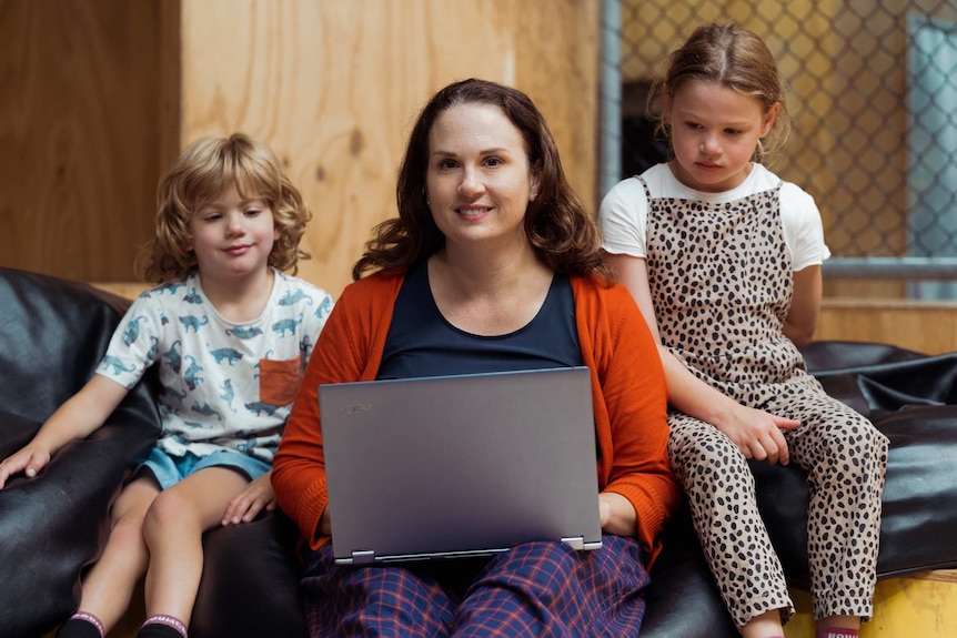 Bailey Bosch holds a lap top while sitting on large beans bags with her children.