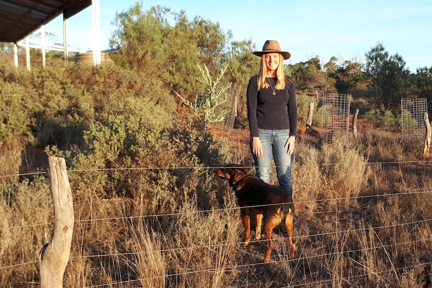 SA ecologist Katherine Moseby standing amongst green shrubs with her dog