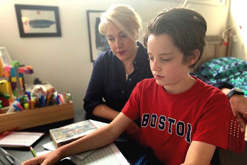 Rupert works on a computer while his mother watches over his shoulder.