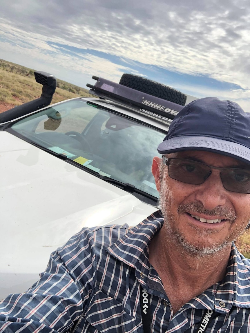 He takes a selfie by his car, wearing a hat