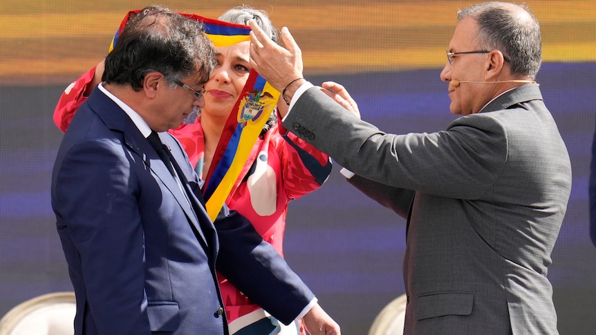 A man and a woman put a red, blue and yellow sash over President Gustavo Petro
