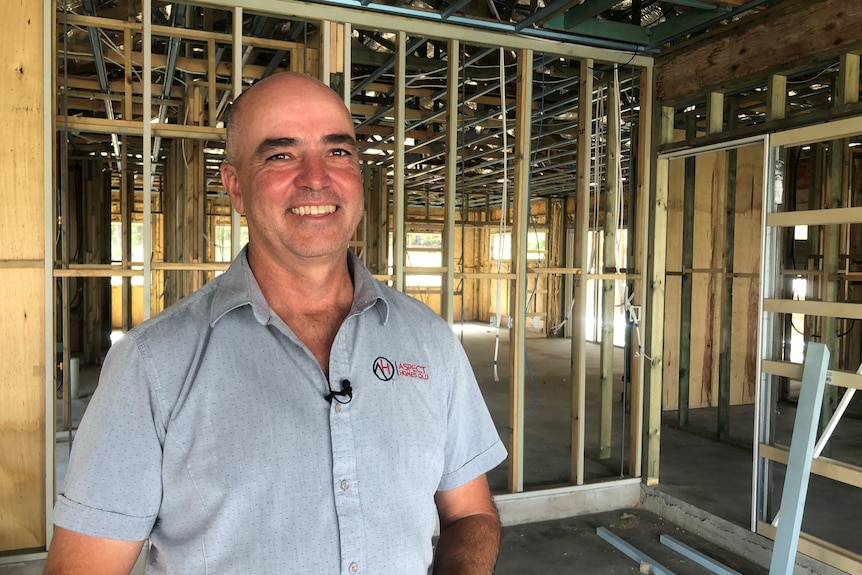 A man stands in a house under construction in front of timber wall frames.