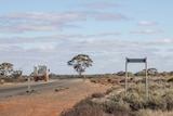 A truck rounds a a bend along a road in outback Western Australia, with a sign for the Kanowna townsite in the foreground.