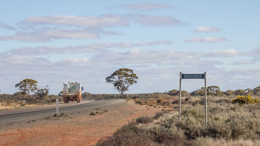 A truck rounds a a bend along a road in outback Western Australia, with a sign for the Kanowna townsite in the foreground.