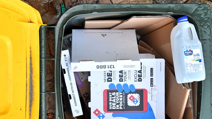 A yellow-top recycling bin with pizza boxes and a milk carton inside.