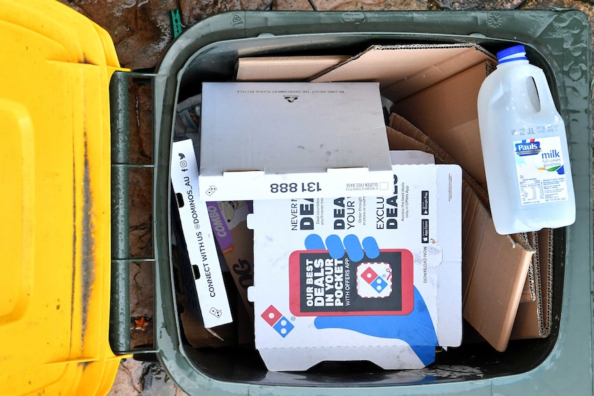 A yellow-top recycling bin with pizza boxes and a milk carton inside.