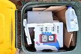 A yellow-top recycling bin with pizza boxes and a milk carton inside.