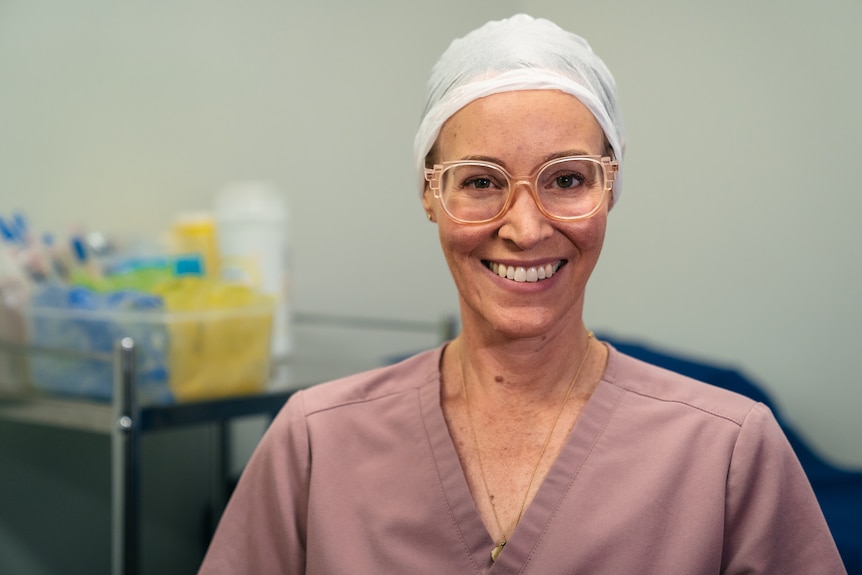 Female doctor wearing muted pink scrubs, glasses and a hair net. 