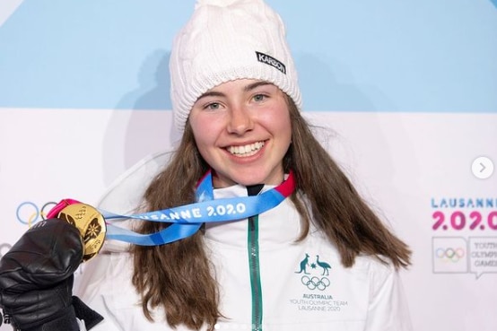 Brunette woman with white beanie and white jacket holding medal