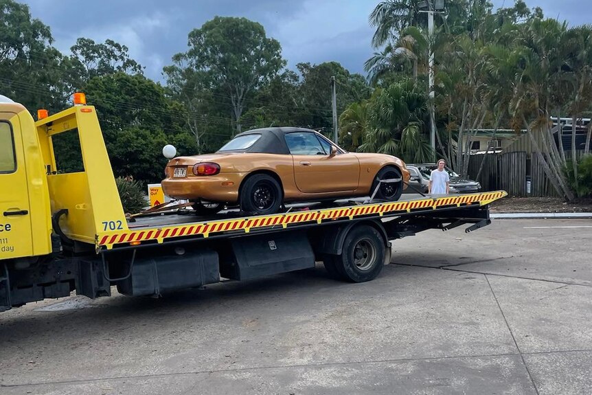 A small bronze sports car on the back of a trailer.