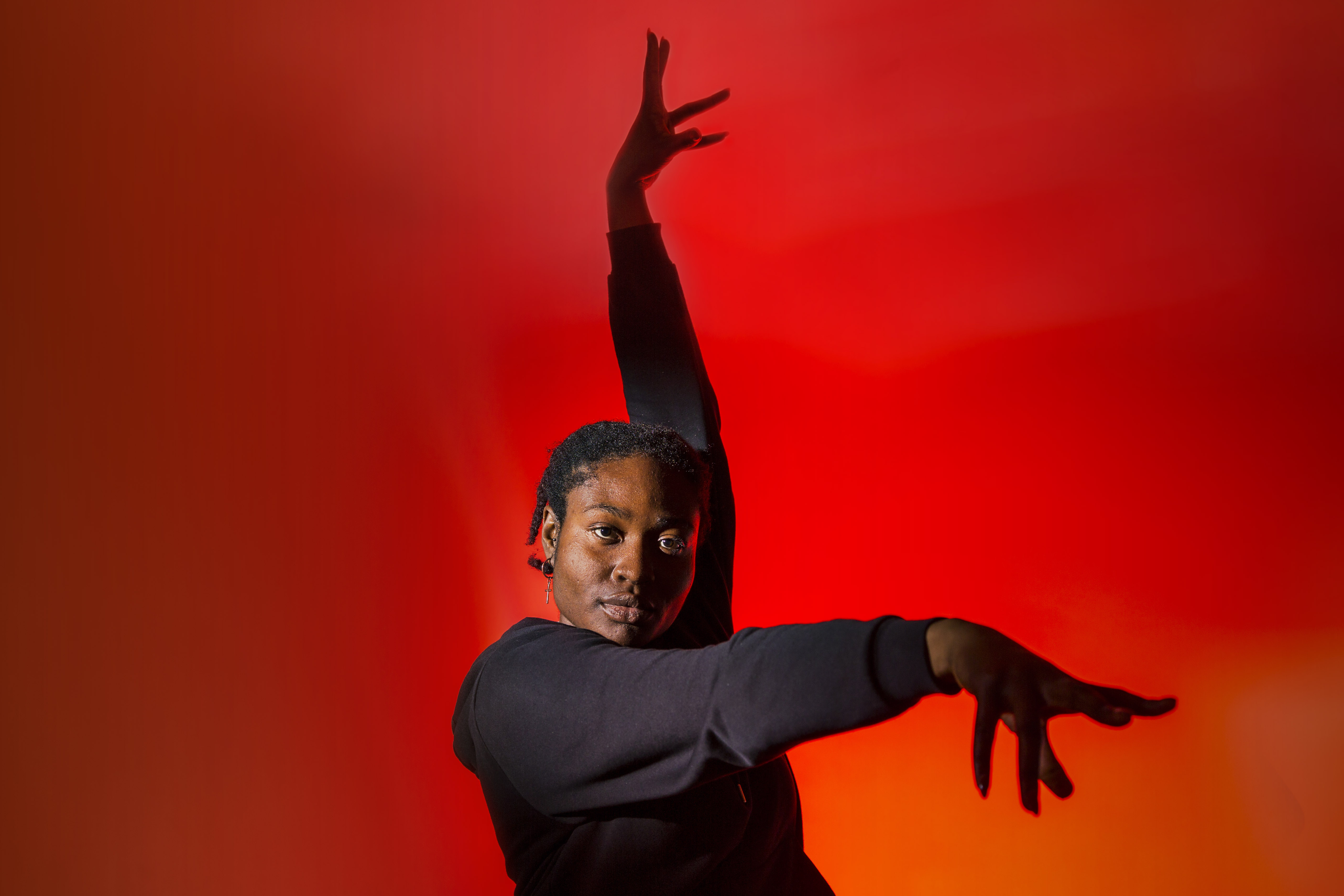Mid-shot colour photograph of dancer and actor Ebube posing in front of a red background.